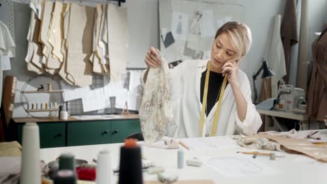 Woman-Tailor-Sitting-At-The-Table-Choosing-Clothes-Pieces-In-Workshop