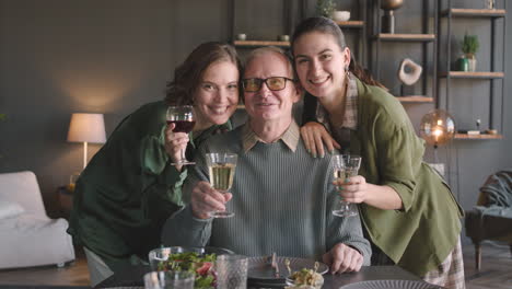 Portrait-Of-A-Happy-Father-And-His-Two-Adult-Daughters-Smiling-And-Toasting-At-Camera-At-Home