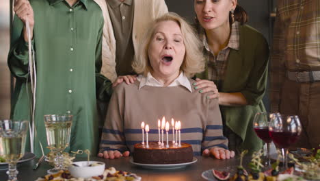 Porträt-Einer-älteren-Frau,-Die-Während-Einer-Feier-Mit-Ihrer-Familie-Zu-Hause-Kerzen-Auf-Einem-Geburtstagskuchen-Ausbläst
