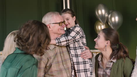 Happy-Grandfather-Holding-His-Granddaughter-And-Blowing-Out-Candles-On-Birthday-Cake-During-A-Celebration-With-His-Family-At-Home