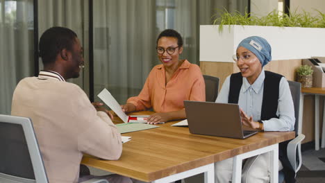 An-Woman-And-A-Muslim-Woman-Co-Workers-Interview-A-Young-Man-Sitting-At-A-Table-In-The-Office-3