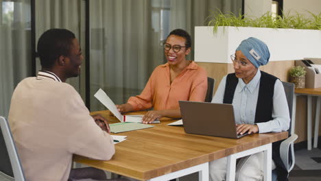 An-Woman-And-A-Muslim-Woman-Co-Workers-Interview-A-Young-Man-Sitting-At-A-Table-In-The-Office-4
