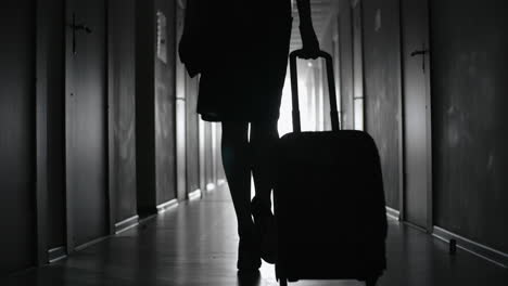 Black-And-White-Rear-View-Of-A-Woman-In-Elegant-Clothes-And-Heels-Carrying-Suitcase-While-Walking-In-A-Hallway