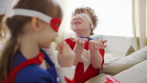 Medium-Closeup-Of-Kids-Putting-On-Superhero-Eye-Masks-Laughing-Out-Loud-While-Parents-Talking-In-Blurred-Background