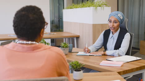 Muslim-Businesswoman-Taking-Notes-Sitting-On-The-Table-While-Talking-With-Her-Coworkers