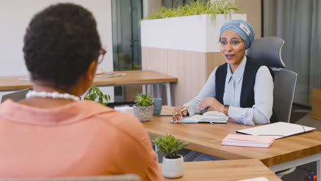 Muslim-Businesswoman-Taking-Notes-Sitting-On-The-Table-While-Talking-With-Her-Business-Partner