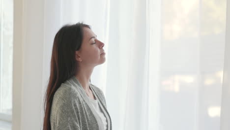 Woman-With-Closed-Eyes-Deeply-Breathing-While-Standing-Near-The-Window-At-Home-In-The-Morning-1