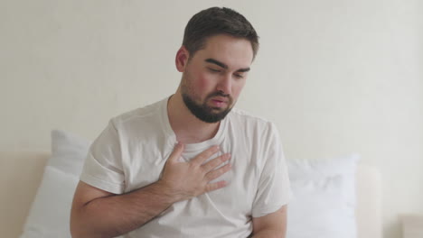 Sick-Man-Sitting-On-Bed-Having-Shortness-Of-Breath-And-Touching-His-Chest