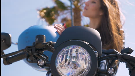 Young-Woman-Sitting-On-Motorcycle-Putting-On-Helmet
