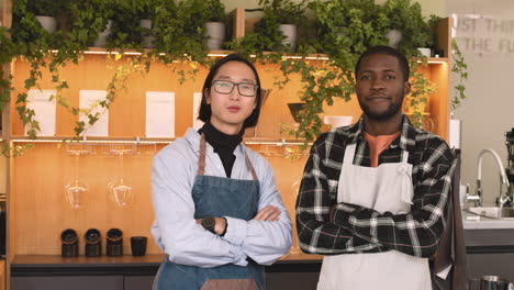 Two-Multiethnic-Waiters-With-Crossed-Arms-Smiling-At-Camera-While-Standing-Behind-Counter-In-A-Coffee-Shop-1