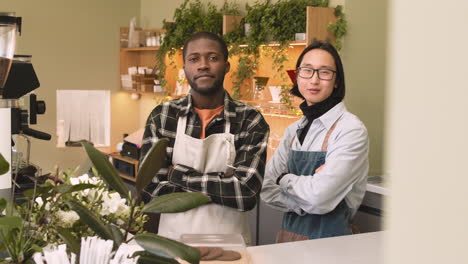 Two-Multiethnic-Waiters-With-Crossed-Arms-Looking-At-Camera-While-Standing-Behind-Counter-In-A-Coffee-Shop-1