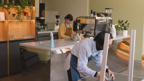 Waiter-Cleaning-Coffee-Shop-Tables-With-Rag,-While-His-Female-Colleague-Cleaning-Countertop