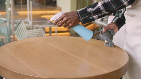 Waiter-Cleaning-Coffe-Shop-Table-With-Disinfectant-Spray-And-Rag-1