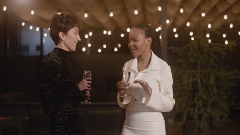 Zwei-Elegante-Multiethnische-Frauen,-Die-Champagnergläser-Halten-Und-Auf-Der-Silvesterparty-Miteinander-Reden