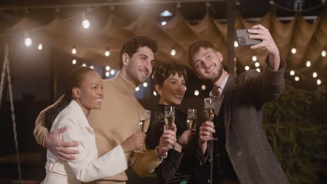 Group-Of-Four-Happy-Multiethnic-Friends-With-Champagne-Glasses-Taking-A-Selfie-Photo-At-New-Year's-Eve-Party