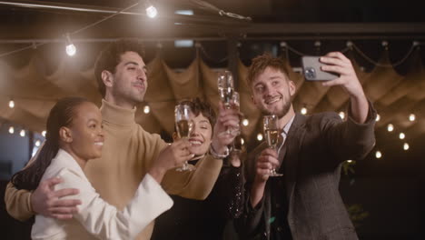 Group-Of-Four-Happy-Multiethnic-Friends-Taking-A-Selfie-Video-And-Toasting-With-Champagne-Glasses-At-New-Year's-Eve-Party-1