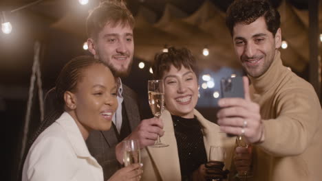 Portrait-Of-Group-Of-Four-Happy-Multiethnic-Friends-Taking-A-Selfie-Video-And-Toasting-With-Champagne-Glasses-At-New-Year's-Eve-Party-3