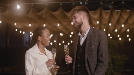 Man-And-Woman-Holding-Champagne-Glasses-And-Talking-To-Each-Other-At-New-Year's-Eve-Party
