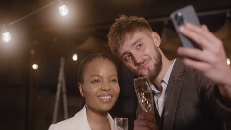 Man-And-Woman-Toasting-With-Champagne-Glasses-While-Taking-A-Selfie-Video-At-New-Year's-Eve-Party-1