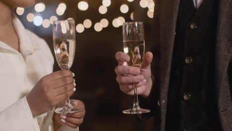 Close-Up-Of-An-Unrecognizable-Multiethnic-Couple-Toasting-With-Champagne-Glasses-At-New-Year's-Eve-Party