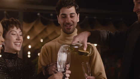 Happy-Man-Pouring-Champagne-In-His-Cheerful-Friends'-Glasses-At-New-Year's-Eve-Party