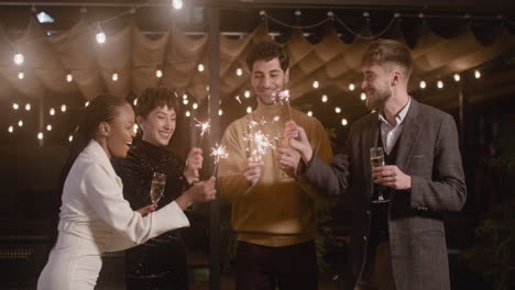 Group-Of-Four-Multiethnic-Friends-Drinking-Champagne-And-Having-Fun-With-Sparklers-At-New-Year's-Eve-Party