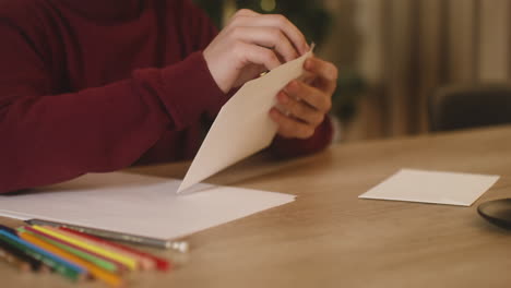 Close-Up-View-Of-A-Child's-Hands-Folding-A-Letter-Of-Wishes-And-Inserting-It-In-A-Evelope-Sitting-At-A-Table