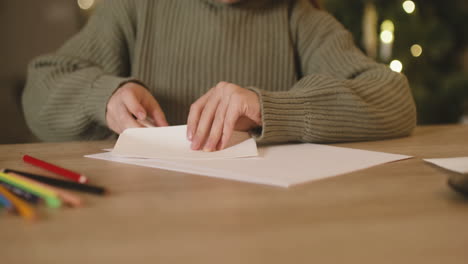 Close-Up-View-Of-A-Girl-In-Green-Sweater-Folding-A-Letter-And-Inserting-It-In-A-Envelope-Sitting-At-A-Table,-Then-Gets-Up-From-The-Chair-And-Leaves-The-Room