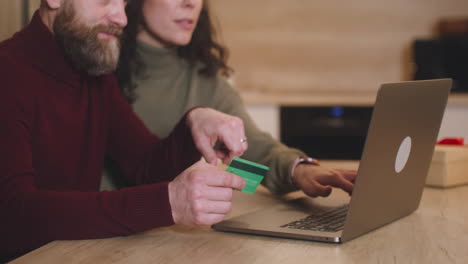 Couple-Buying-Online-With-A-Credit-Card-Using-A-Laptop-Sitting-At-A-Table-Near-A-Present