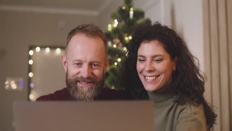 Front-View-Of-A-Couple-Using-A-Laptop-In-A-Room-Decorated-With-A-Christmas-Tree
