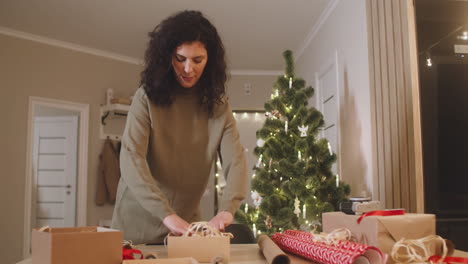 Brünette-Frau,-Die-Weihnachtsgeschenke-Auf-Einem-Tisch-In-Einem-Mit-Einem-Weihnachtsbaum-Geschmückten-Raum-Einwickelt-1