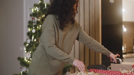 Brünette-Frau,-Die-Weihnachtsgeschenke-Auf-Einem-Tisch-In-Einem-Mit-Einem-Weihnachtsbaum-Geschmückten-Raum-Einwickelt-2