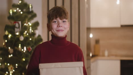 Vorderansicht-Eines-Blonden-Jungen-In-Einem-Roten-Rollkragenpullover,-Der-Geschenke-In-Einem-Mit-Einem-Weihnachtsbaum-Geschmückten-Raum-Hält-1