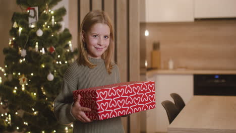 Front-View-Of-A-Blonde-Girl-In-Green-Sweater-Holding-Gifts-In-A-Room-Decorated-With-A-Christmas-Tree