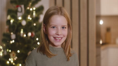 Front-View-Of-A-Blonde-Girl-Smiling-At-Camera-In-A-Room-Decorated-With-A-Christmas-Tree