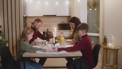 Paar-Und-Ihre-Kinder-Beten-Und-Segnen-Den-Tisch-Vor-Dem-Weihnachtsessen-Mit-Der-Familie
