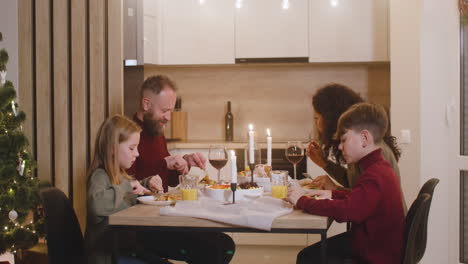 Family-Of-Parents-And-Two-Siblings-Having-Dinner-At-Christmas-Sitting-At-The-Kitchen-Table