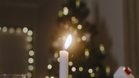 Die-Kamera-Fokussiert-Auf-Eine-Brennende-Kerze,-Im-Hintergrund-Steht-Ein-Weihnachtsbaum-Mit-Verschwommenen-Lichtern