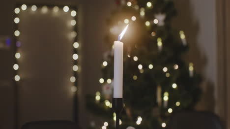 Die-Kamera-Fokussiert-Auf-Eine-Brennende-Kerze,-Im-Hintergrund-Steht-Ein-Weihnachtsbaum-Mit-Verschwommenen-Lichtern-1