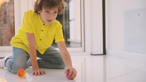 Blond-Boy-With-Curly-Hair-Kneeling-On-The-Floor-While-Playing-With-Balls-With-His-Dog