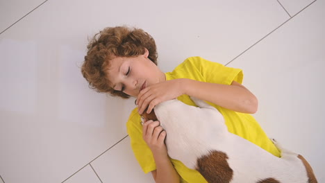 Top-View-Of-A-Blond-Boy-With-Curly-Hair-Lying-On-The-Floor-And-Caresses-His-Dog-1