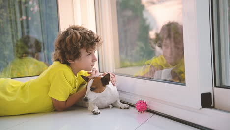 Blond-Boy-With-Curly-Hairs-Lying-On-The-Floor-With-His-Dog-While-Caresses-Him-And-Looking-Out-The-Window-2
