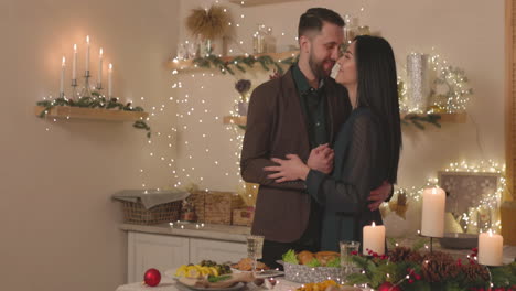 Elegant-Couple-Standing-At-Christmas-Dinner-Table-And-Tenderly-Embracing-Each-Other-While-Woman-Looking-At-Camera