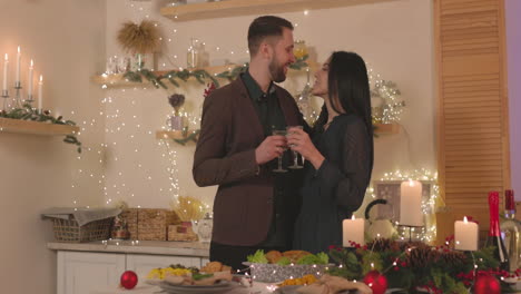 Loving-Couple-Standing-At-Christmas-Dinner-Table,-Holding-Champagne-Glasses-And-Tenderly-Embracing-Each-Other
