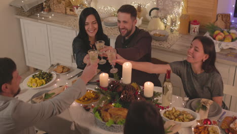 Gruppe-Glücklicher-Freunde,-Die-Am-Tisch-Sitzen-Und-Anstoßen,-Bevor-Sie-Das-Weihnachtsessen-Zu-Hause-Essen