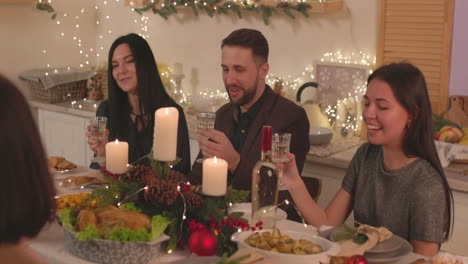 Group-Of-Happy-Friends-Sitting-At-Table,-Holding-Champagne-Glasses-And-Talking-To-Each-Other-At-Home-On-Christmas-1