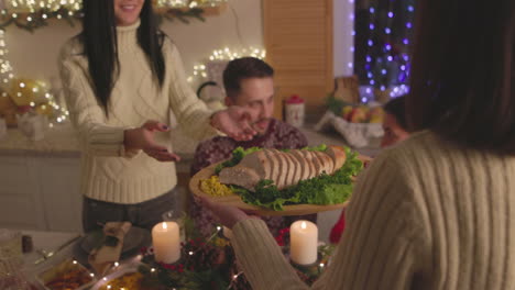 Woman-Passing-A-Tray-With-Sliced-Bread-To-Her-Friend-During-Christmas-Dinner