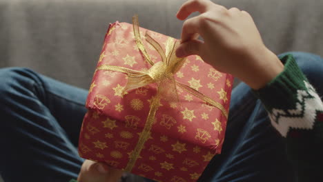 Draufsicht-Auf-Ein-Nicht-Erkennbares-Kind,-Das-Auf-Dem-Sofa-Sitzt-Und-Mit-Der-Weihnachtsgeschenkbox-Spielt