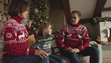 Cute-Little-Girl-Sitting-With-Her-Parents-On-Sofa-And-Giving-Christmas-Gift-To-Her-Loving-Father