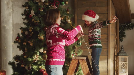 Glückliche-Mutter-Und-Tochter-Tanzen-Und-Spielen-Zusammen-Mit-Lichtern,-Während-Sie-Zu-Hause-Den-Weihnachtsbaum-Schmücken
